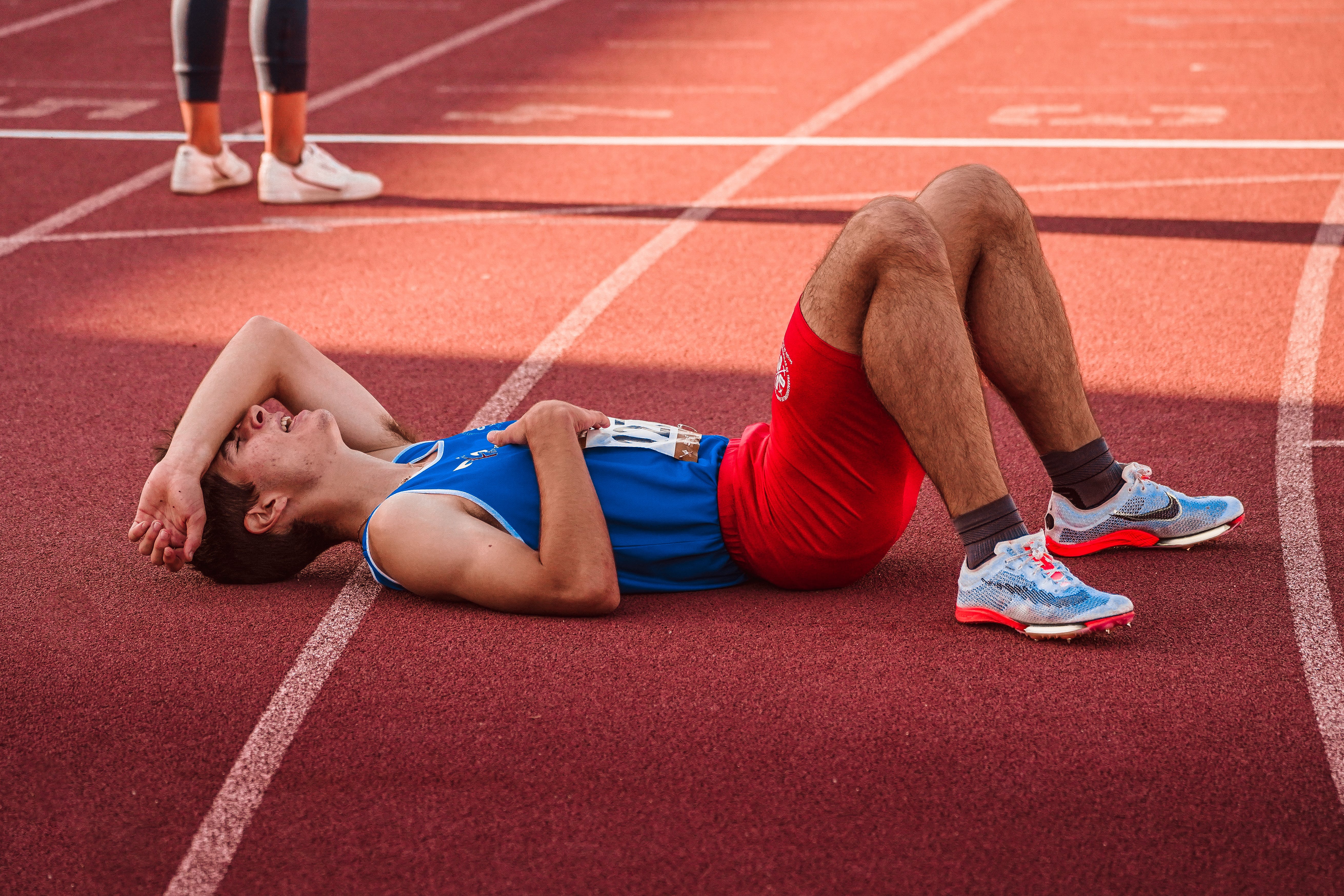 A runner in blue shirt and orange spandex lying on the track tired.