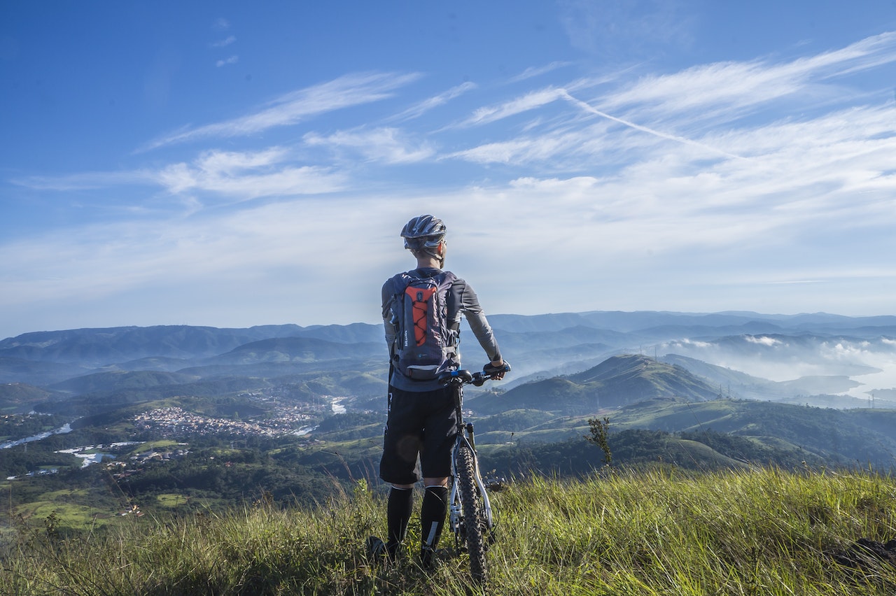 A cyclist on a grassy ledge overlooking a mountainous view